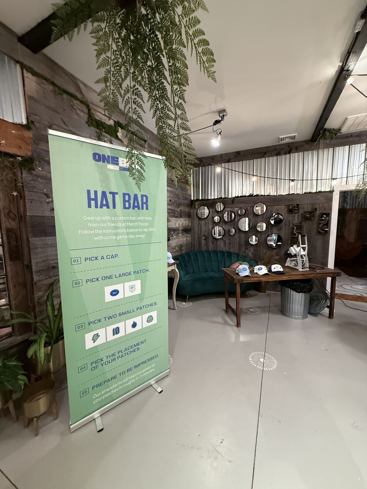 Display shelf showing sample decorated hats and promotional items on a pegboard backdrop in an event booth
