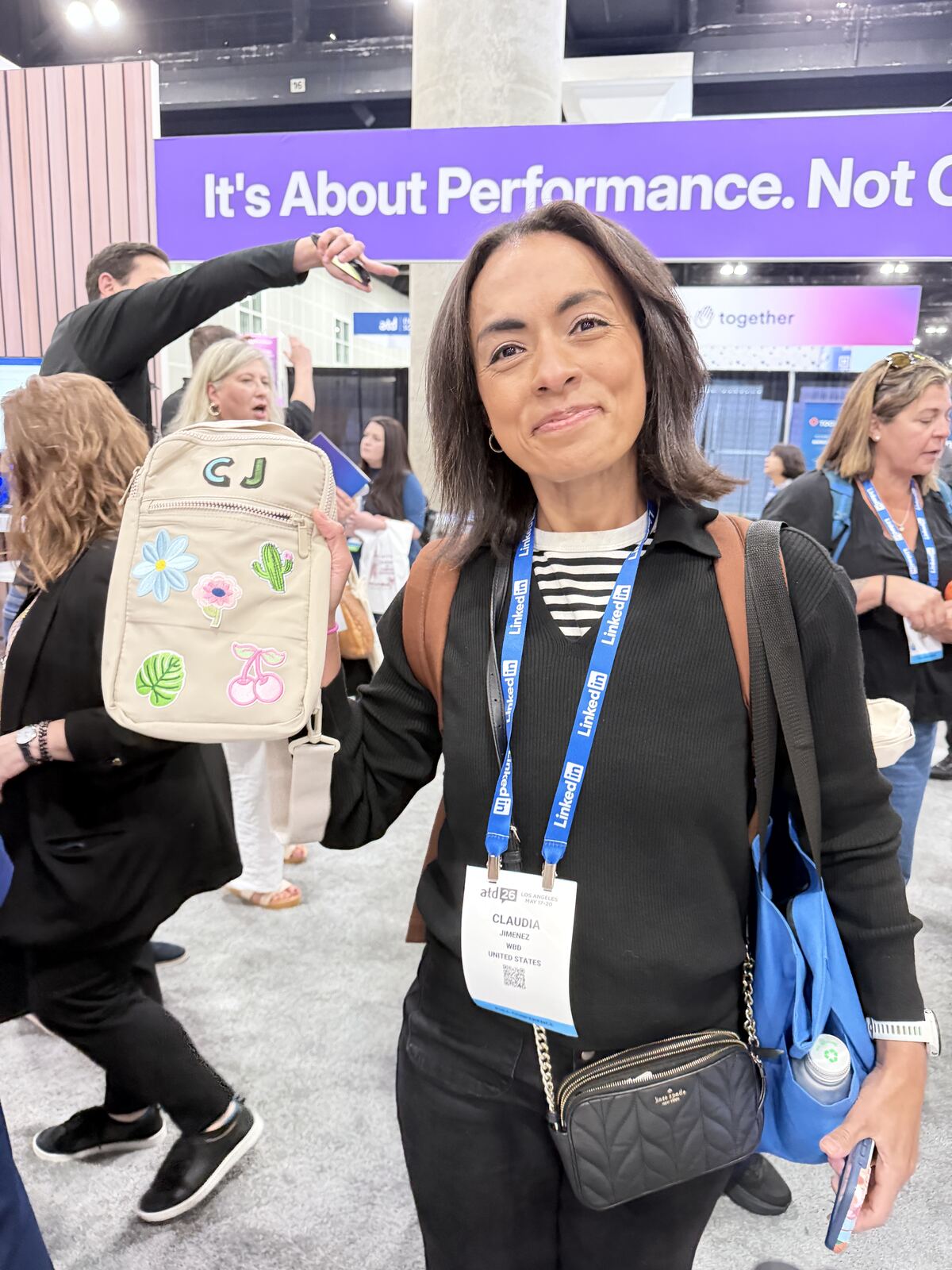 Woman holding a customized tote bag with embroidered patches at an event with signage visible
